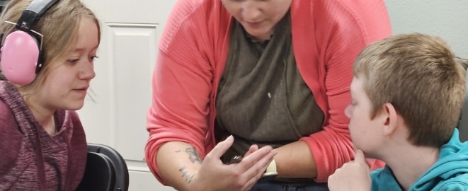 Educator showing a small animal to two children during an indoor nature education class.