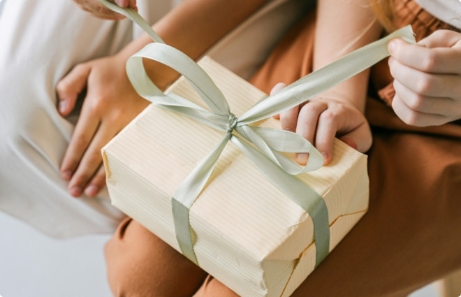 Close-up of hands tying a pale green ribbon around a wrapped gift box.