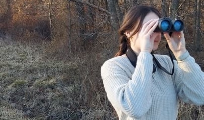 Woman using binoculars to observe wildlife in a wooded natural area.